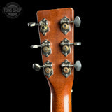 Close-up of the headstock of an acoustic guitar with six tuning pegs and decorative metal tuners on a black background. A Tone Shop watermark is visible in the top left corner.