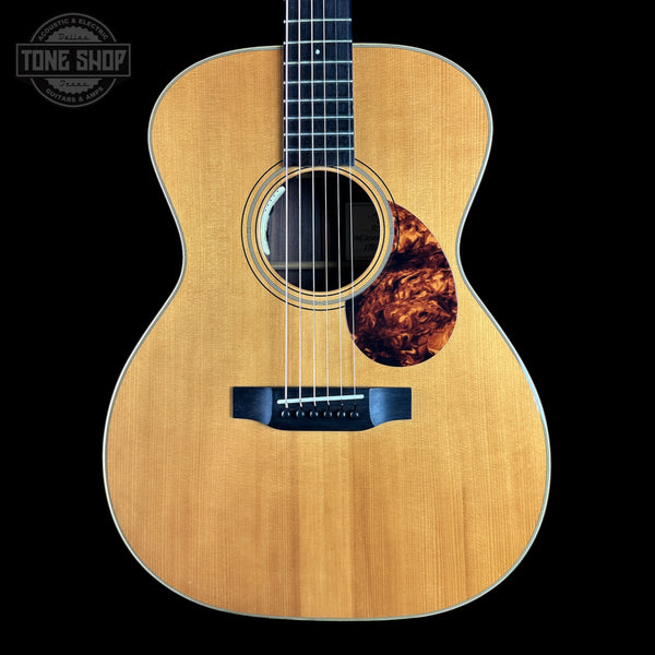 A front-facing acoustic guitar with a natural wood body, black neck, and a tortoiseshell-style pickguard, shown against a solid black background. A 'TONE SHOP' watermark is visible in the top-left corner.