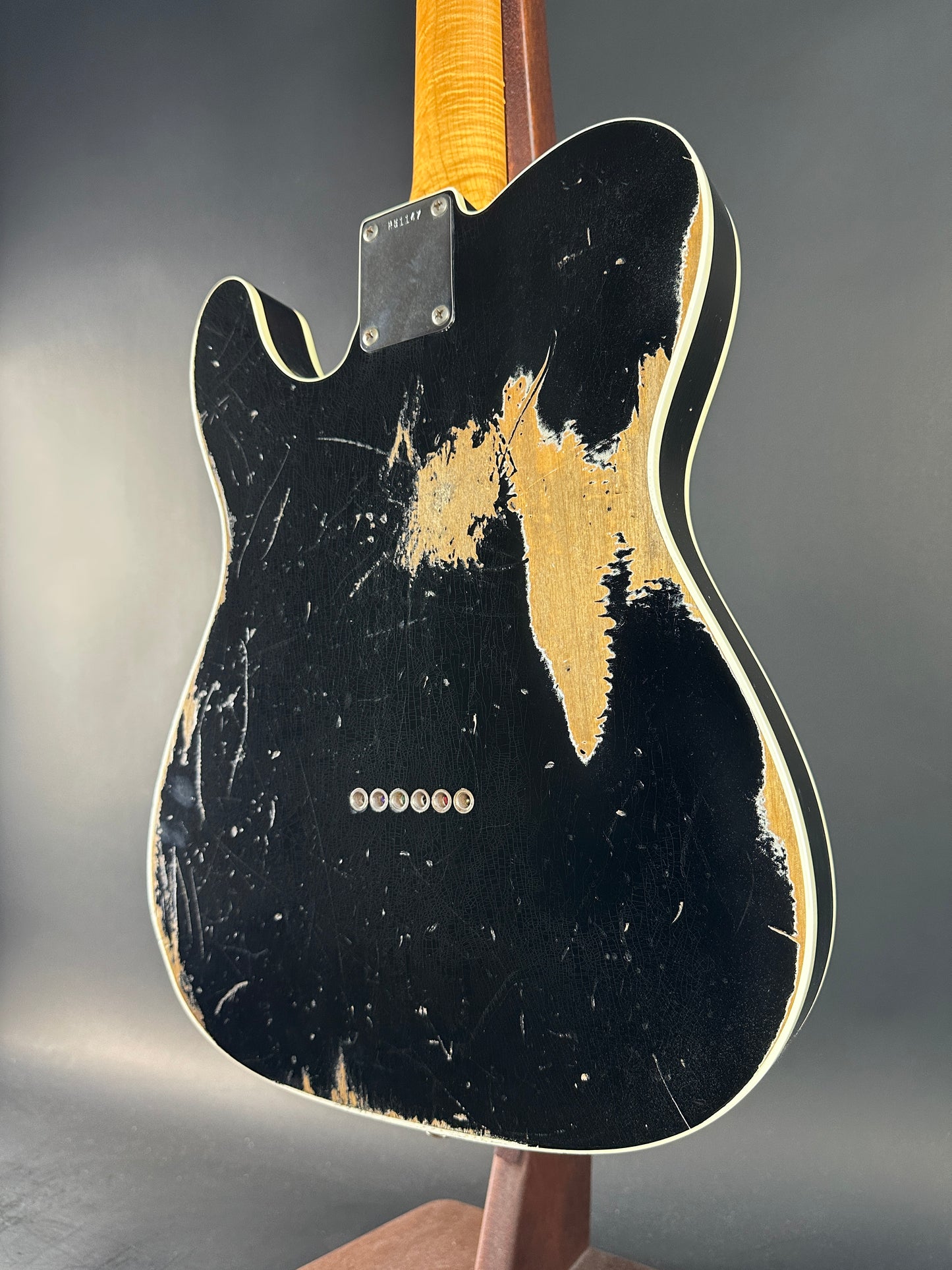 Distressed black electric guitar with gold pickguard on a gray background