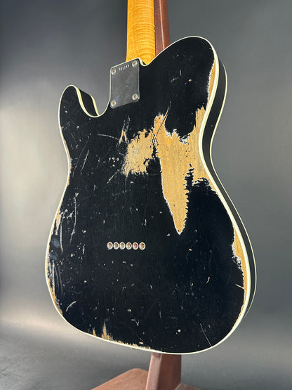 Distressed black electric guitar with gold pickguard on a gray background