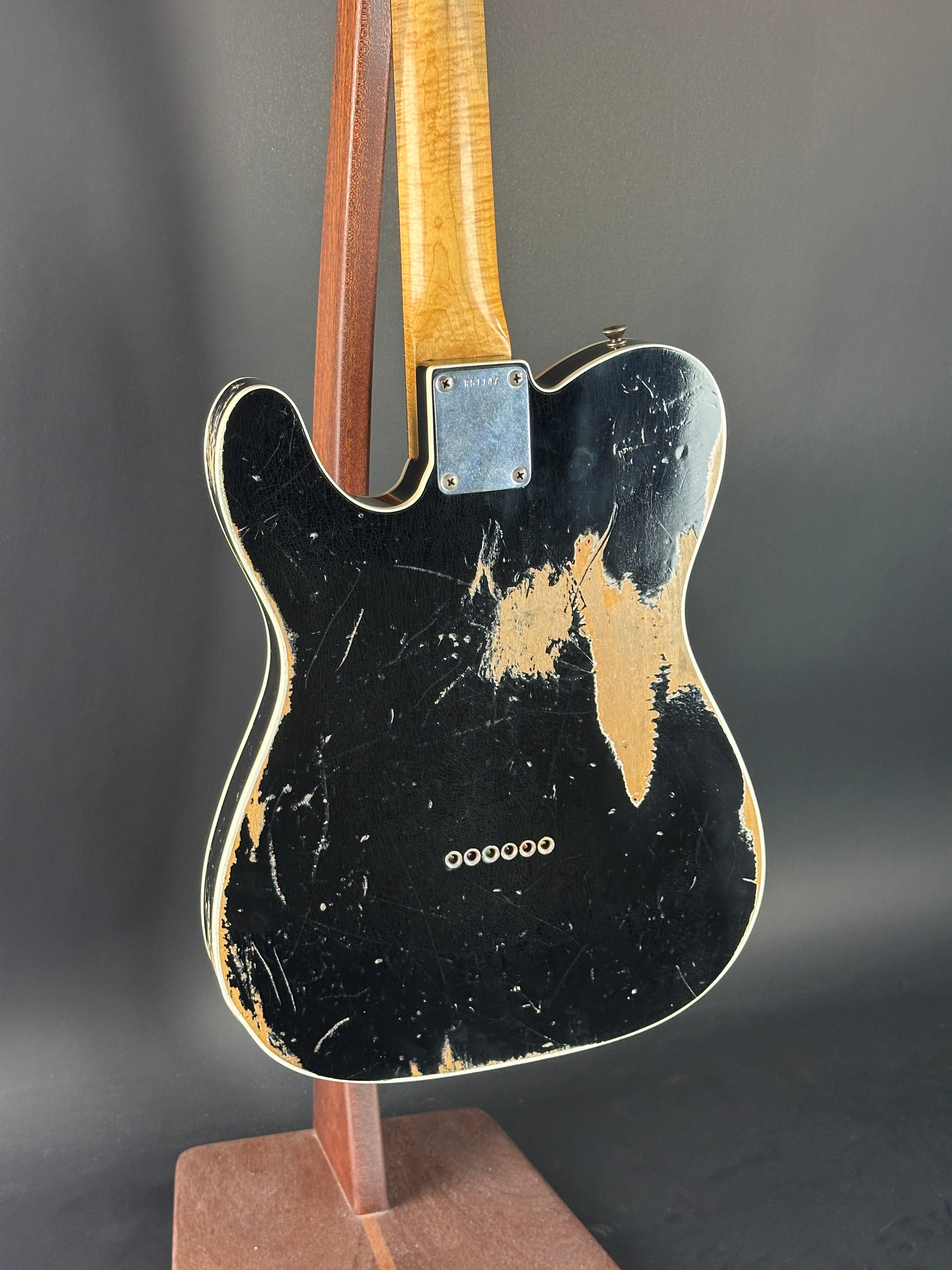 Back of a Fender electric guitar with a worn finish on a dark background