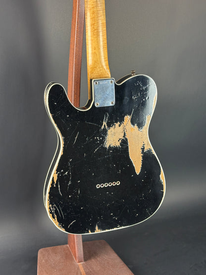 Back of a Fender electric guitar with a worn finish on a dark background