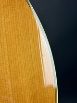 Close-up detail of a guitar body showing the natural wood grain finish and the edge of the soundhole surround against a dark background.