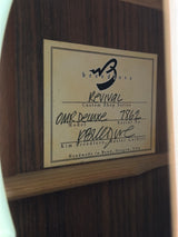 A close-up of a custom guitar headstock label inside a dark wood headstock, featuring the brand 'Bravo' and handwritten model details.
