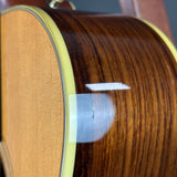 Close-up of an acoustic guitar body showing the dark brown wood grain back, a light natural wood soundboard, and a white circular reflection on the glossy finish.