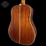 Back view of a wooden acoustic guitar with a visible brand logo in the corner.