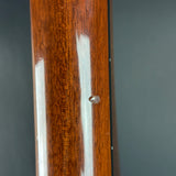 Close-up of a polished reddish-brown wooden surface with visible wood grain, a small metallic rivet or screw head, and two vertical white streaks on a dark gray background.