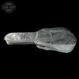 A dark gray padded guitar or ukulele case shown from the side on a black background, with a small red and white Tone Shop logo patch near the headstock end.