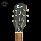 Close-up of a Fender electric guitar headstock, showing the black wood finish, white Fender logo, six gold tuning pegs, and the neck beginning below, set against a solid black background.