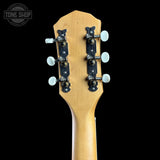 Close-up of the headstock of a guitar with a natural wood finish and black tuning pegs, shown against a solid black background with a Tone Shop watermark in the top left corner.