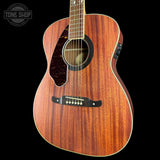 A close-up of a Taylor acoustic guitar body with a rich reddish-brown wood grain finish, black pickguard, and white binding, shown against a solid black background with a Tone Shop watermark in the top-left corner.