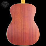The back of an acoustic guitar made of reddish-brown wood with a visible grain pattern, shown against a solid black background. A Tone Shop watermark is visible in the top-left corner.