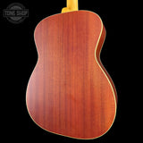 The back of an acoustic guitar with a rich reddish-brown wood finish and a light-colored neck, shown against a solid black background with a Tone Shop watermark in the top left.
