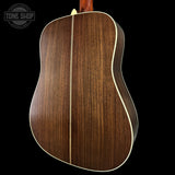 Back view of a wooden acoustic guitar with a visible brand logo in the corner.