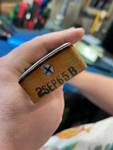Hand holding a wooden block with '2SEP65B' engraved, blurred background