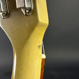 Close-up of the headstock of an electric guitar, showing the back side with silver tuning pegs and a light cream-colored body finish against a dark gray background.