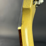 Close-up detail of an electric guitar headstock and upper body, showing a glossy pale yellow finish, dark wood fretboard, and silver tuning pegs against a dark gray background.