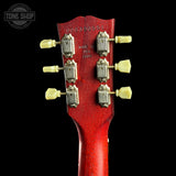 Close-up of the headstock of a red acoustic guitar against a black background, showing six silver tuning machines with cream-colored knobs. A Tone Shop watermark is visible in the top left corner.