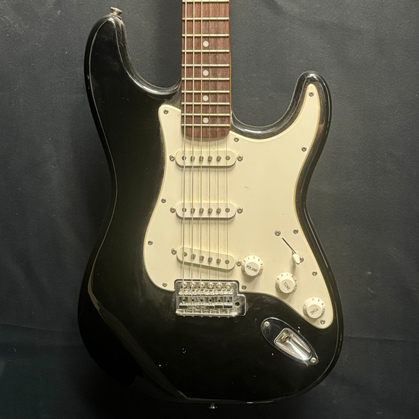 Black electric guitar with a white pickguard on a dark background
