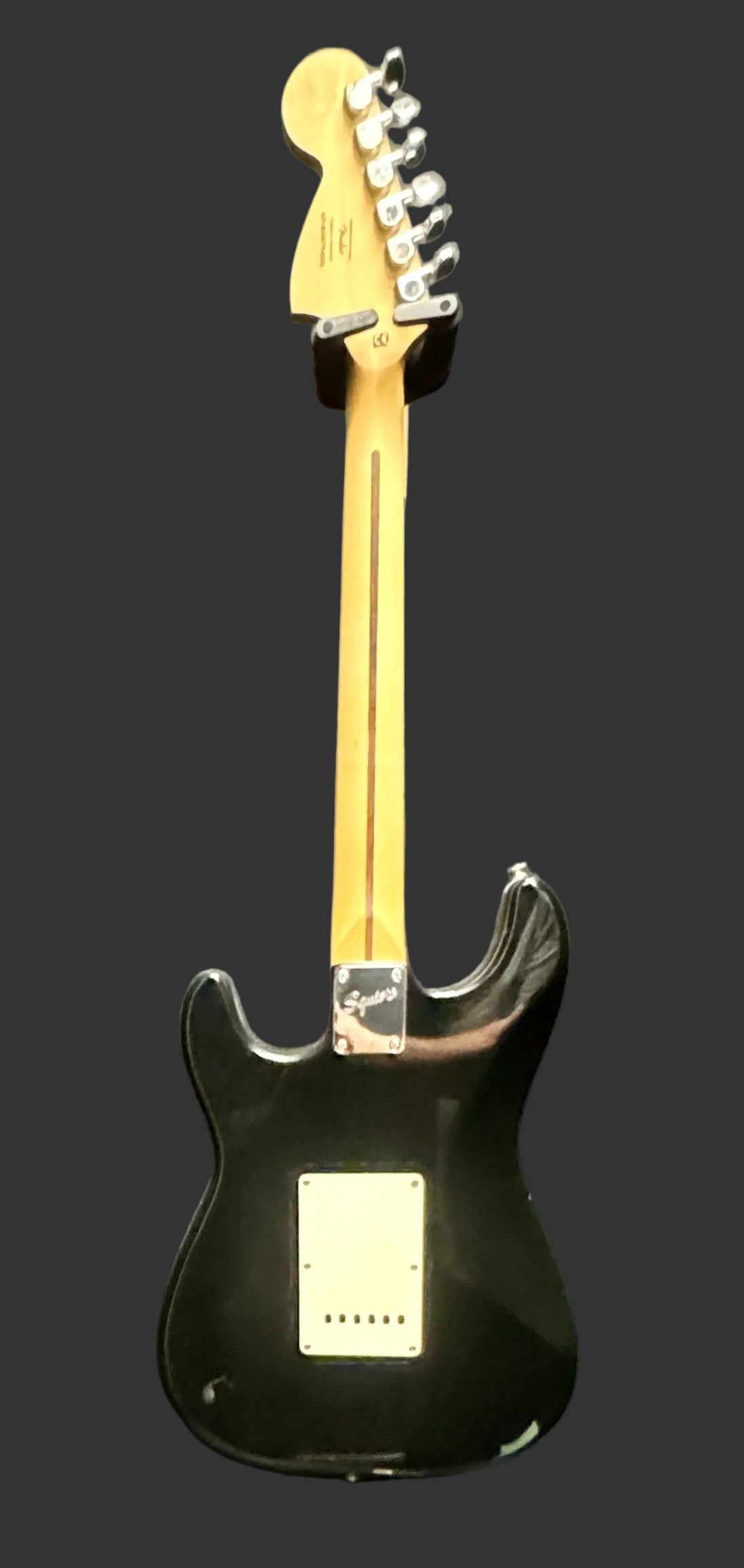 Black electric guitar with a pickguard on a gray background