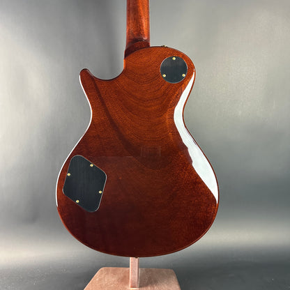 Back view of a wooden electric guitar on a stand with a gray background