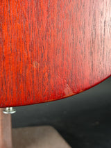 Close-up of a reddish-brown wood grain surface with a curved edge and a small silver screw visible against a dark background.