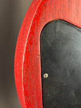 Close-up detail of a red wood-grain guitar body with a black pickguard and a small silver screw.