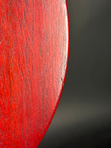 Close-up of a glossy red wooden object with visible wood grain and a curved edge against a dark gray background.
