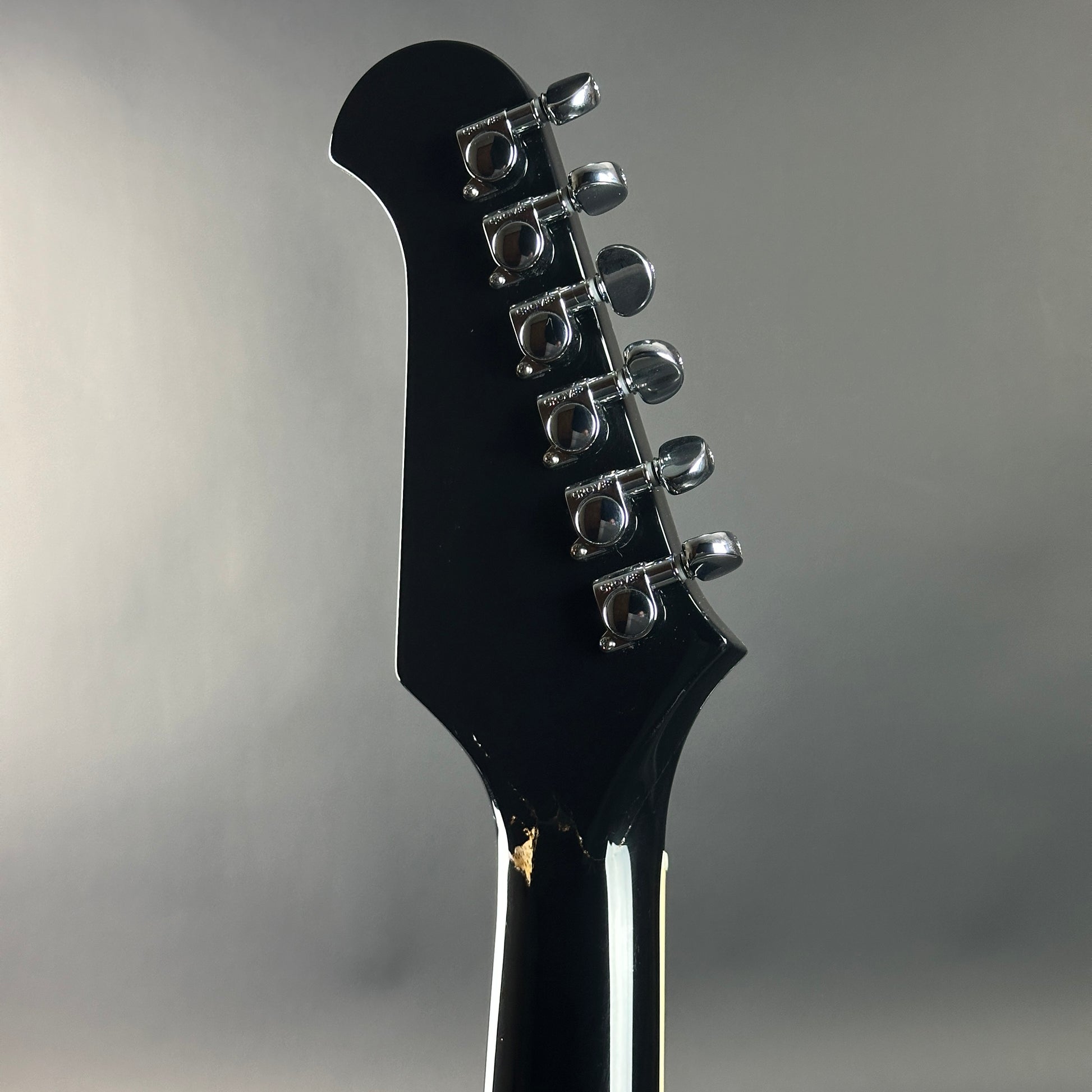 Close-up of a black guitar headstock with tuning pegs on a gray background
