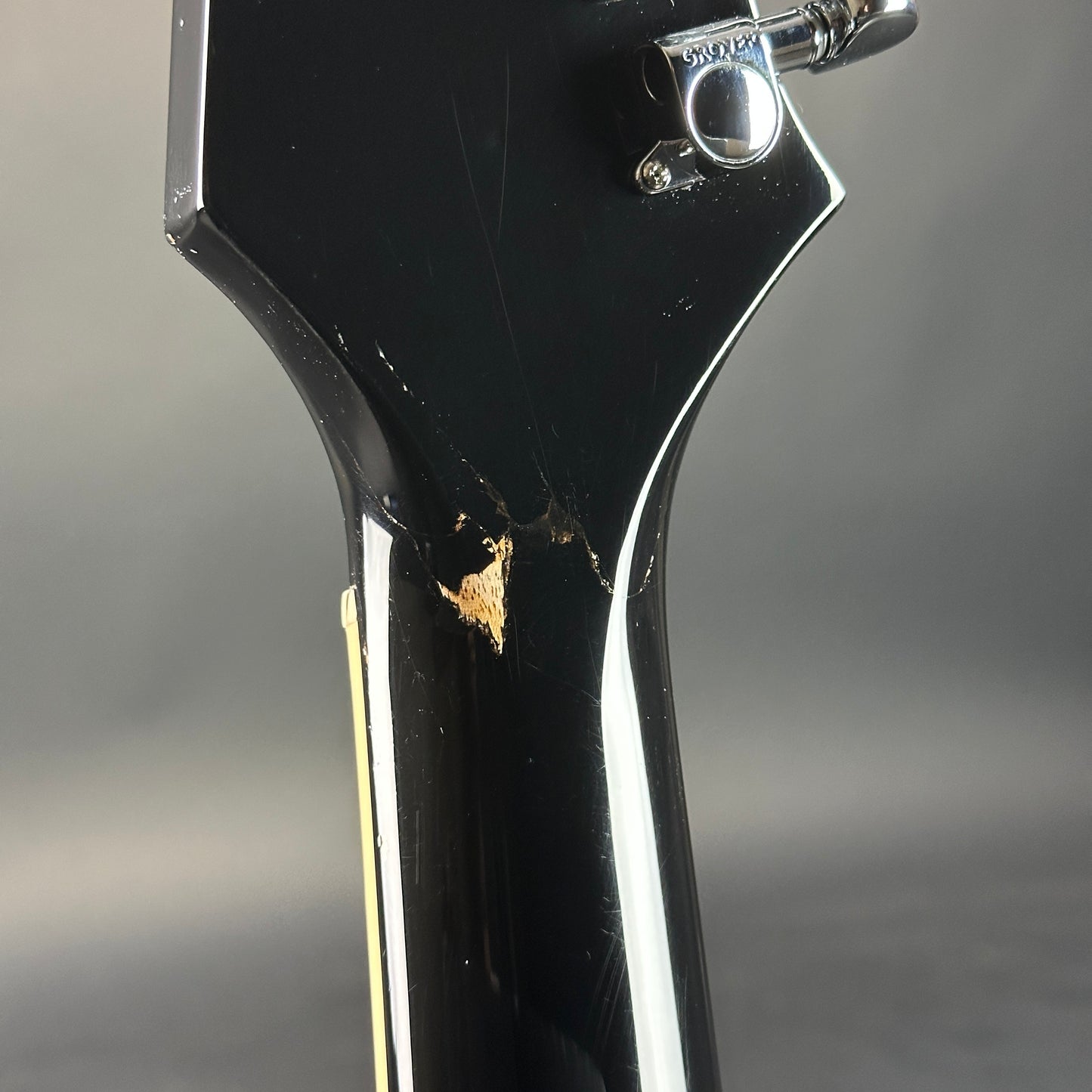 Close-up of a black guitar neck with a scratch on a gray background