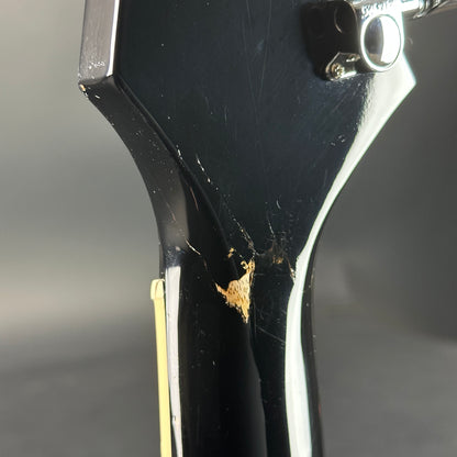 Close-up of a black guitar neck with visible damage on a gray background