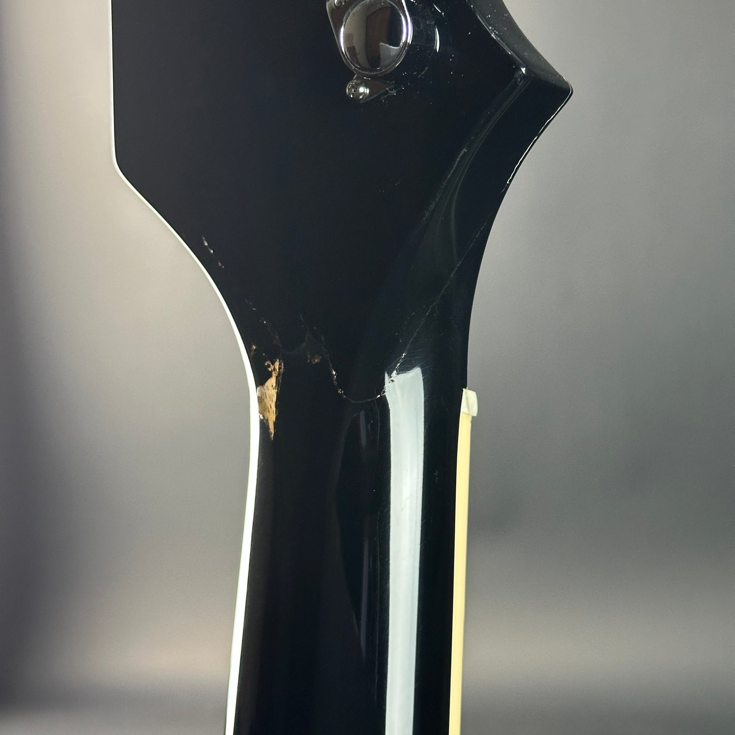 Close-up of a black electric guitar neck with a blurred gray background