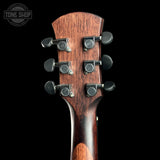 Close-up of the headstock of a six-string acoustic guitar, showing a dark brown wood grain finish and four black tuning pegs, set against a solid black background with a Tone Shop watermark in the top left corner.