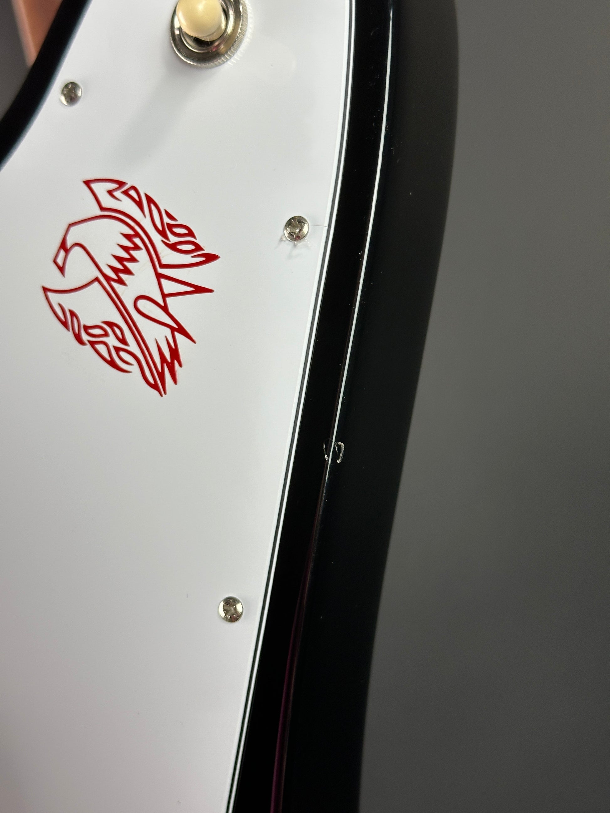 Close-up of a guitar headstock with a red logo on a gray background