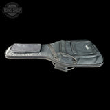 A dark gray padded guitar or bass instrument case with multiple zippered pockets and a shoulder strap, shown against a solid black background. A Tone Shop watermark is visible in the top-left corner.