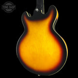 Close-up of the back of an electric guitar body showing a classic sunburst finish that transitions from bright amber-orange in the center to dark brown and black around the edges, set against a solid black background.