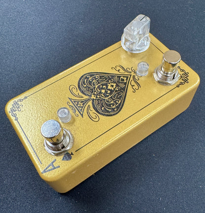 Gold guitar effects pedal with aace of spades design on a dark background