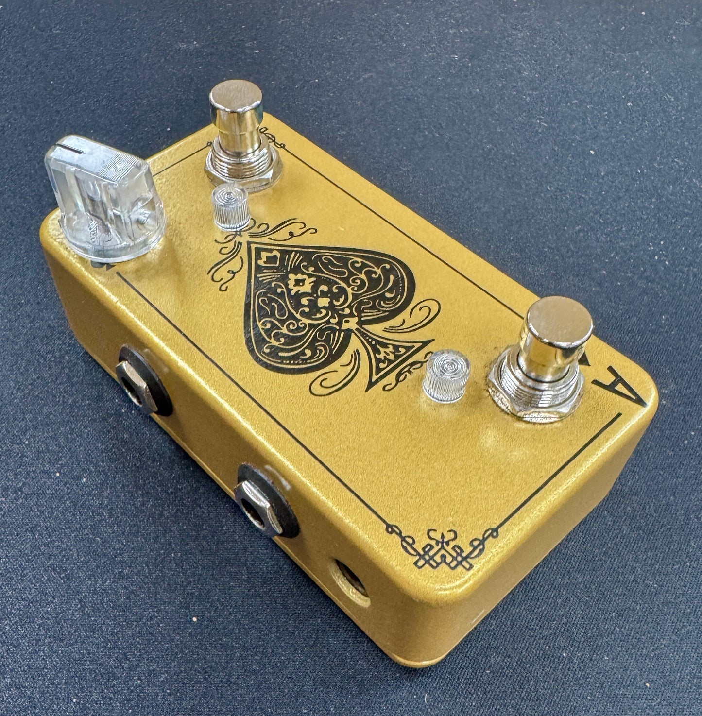 Gold guitar effects pedal with intricate design on a dark surface