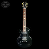 A black electric guitar with a dark brown fretboard and gold tuning pegs, shown vertically against a solid black background. A circular 'TONE SHOP' watermark is visible in the top-left corner.