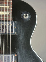 Close-up of a black electric guitar body showing a single switch, pickups, and part of the fretboard against a neutral gray background.