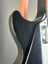 Close-up of the lower body of an electric guitar, showing a black glossy body with visible scratches and a silver hardware plate.
