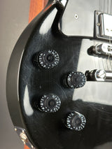 Close-up of a glossy black electric guitar body showing four black control knobs with white markings, part of the silver hardware, and a small section of wood fretboard.