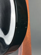 Close-up of a glossy black curved object, likely a bowl or dish, showing a small chip or scratch on the rim against a neutral gray background with a brown surface above.