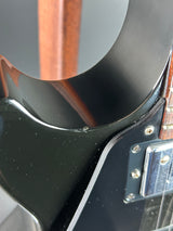 Close-up of a glossy black electric guitar body with a wood neck visible at the top and a chrome hardware plate.