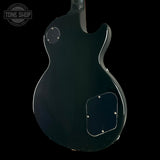The rear view of a black electric guitar body, photographed against a solid black background. A circular 'TONE SHOP' watermark is visible in the upper left corner.
