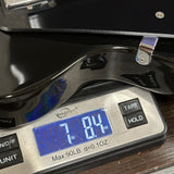 A close-up of a glossy black guitar body resting on a digital scale displaying 7.84 lbs.