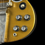 Close-up of a gold metallic electric guitar body showing four black and silver control knobs, a silver bridge, and a black switch against a black background.