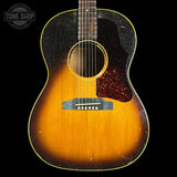 A vintage acoustic guitar with a classic sunburst finish, featuring a dark black outer edge fading to a warm golden-orange center, set against a solid black background.