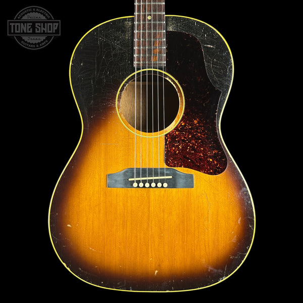 A vintage acoustic guitar with a classic sunburst finish, featuring a dark black outer edge fading to a warm golden-orange center, set against a solid black background.