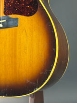 Close-up of the back of a sunburst acoustic guitar showing the wood grain, binding, and part of the dark pickguard.